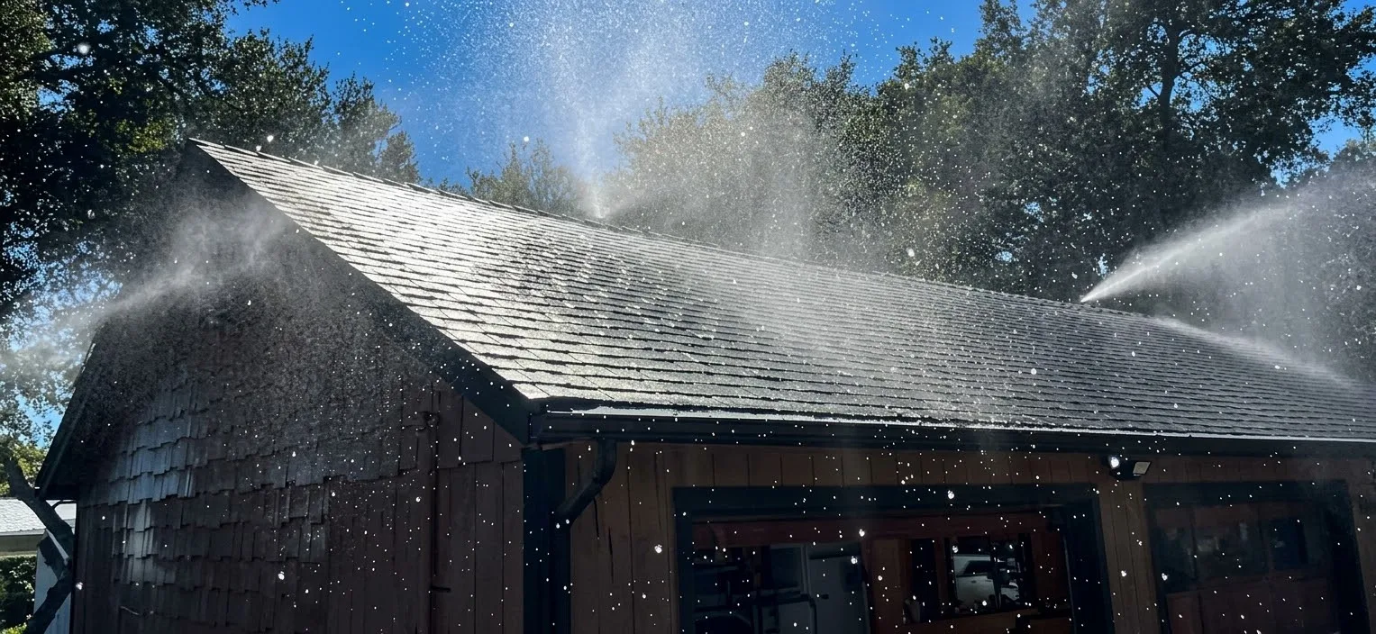 FireRoofs roof sprinklers spraying water across the shingle roof of a Bay Area home and garage under oak trees